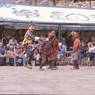 The hunter Gonpo Dorje beating his servant Acho Pento while other atsara are looking on, dance of Milarepa (Sha ba sha khyi 'cham), Paro Tshechu (tshes bcu), dance arena, Paro Tshechu (tshes bcu), 2nd day