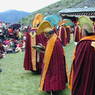 A line of monks wearing yellow hats processing around the courtyard.