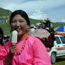 A Tibetan woman wearing a pink shirt and eating a popsicle.
