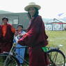 A long haired Tibetan man walking his bicycle.
