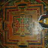 Small statues in front of a mural of a mandala.